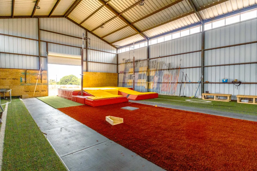 Inside the Off The Grid Pole Vault facility: runway, pit, and pole rack